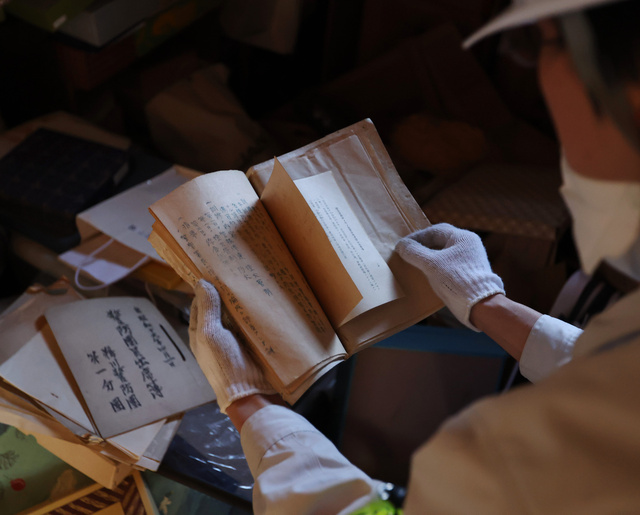 傾いた土蔵の中で、戦前に書かれたとみられる古文書を確認する関係者=2024年3月30日午後、石川県能登町、林敏行撮影