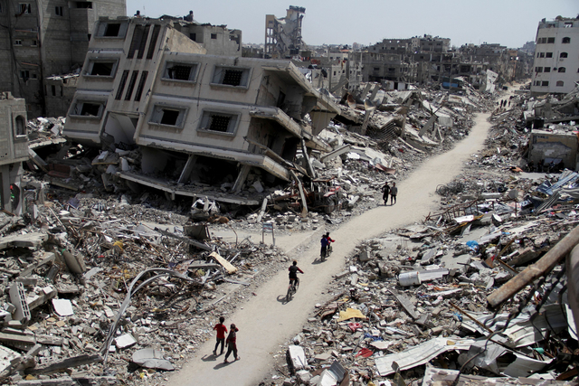 3月31日、パレスチナ自治区ガザでイスラエル軍の作戦で壊れた建物の前を自転車に乗って通る人たち=ロイター