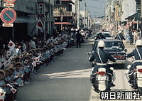 徳之島町役場近くの商店街で、日の丸を手にした園児たちの前を進む皇太子さまの車列