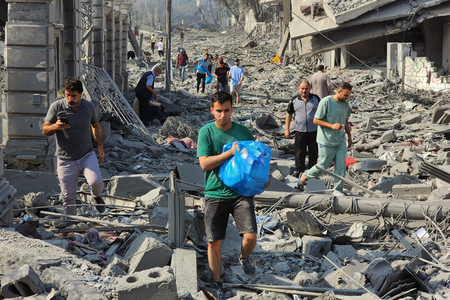 ガザ地区で2023年10月10日、イスラエルの空爆により破壊された場所を歩くパレスチナ人ら=AP
