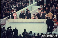 万博開会式で、帽子を振る昭和天皇。右は香淳皇后、左に皇太子さま、美智子さま