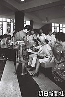 フィリピン大学家政学部で、披露された民族衣装に興味津々な様子で風合いを確かめ、女子学生に話しかける美智子さま