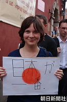 ワルシャワ歴史地区で、画用紙に描いた「日の丸」に「日本が一番。」の文字を記した手作りのボードを持って歓迎する若い女性