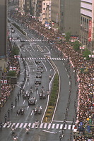 沿道を埋めた人たちの祝福を受けながら進む、皇太子さまと雅子さまのパレードの車列。道路の両側には警備の警官が長い人間の壁を作った＝９３年６月９日、東京・麹町の新宿通りで