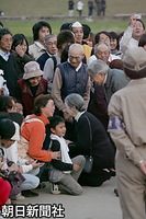 川口中学校で、地面に座って迎えた住民にひざをついて親しく会話される皇后さま、それを見守る天皇陛下