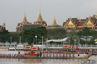 パレードでバンコク中心部を流れるチャオプラヤー川を進む伝統装束を着た海軍の兵士が櫂をこぐ王室御座船。後方は王宮