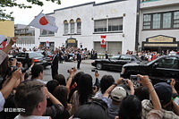 バンクーバー市のダウンタウンで日本人街にあるアレキサンダー・ストリートに面したバンクーバー日本語学校・日系人会館を出発する天皇、皇后両陛下の車列。日の丸とカナダ国旗、それにカメラを手にした大勢の日系人