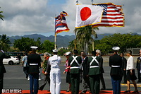 星条旗、日の丸、ハワイ州旗を持つ儀仗隊の前を進まれる天皇、皇后両陛下。首には歓迎のレイがかけられている。右端はリンダ・リングル・ハワイ州知事