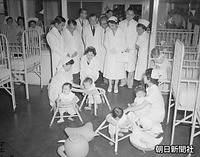 児童福祉を学ぼうと母子愛育会を訪れ、赤ちゃんをあやす美智子さま。左は皇太子さま、右後ろは同会総裁の三笠宮妃百合子さま